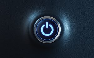 A glowing blue power button with a metallic rim set against a dark, textured background. The button is illuminated, symbolising power or activation.