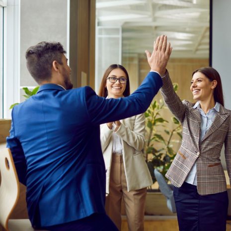 Three business professionals celebrating success in a modern office after completing a training program